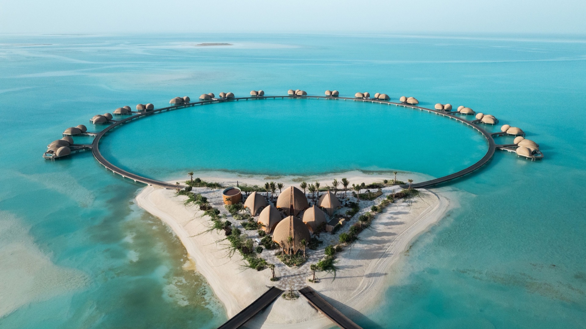 Aerial view of overwater villas arranged in a ring above a turquoise Red Sea lagoon